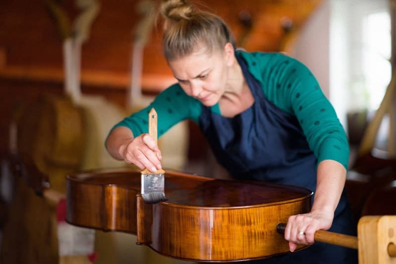 Ecaterina applying varnish to a cello with a brush